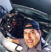 Leo smiling in front of an open hood, wearing work gloves